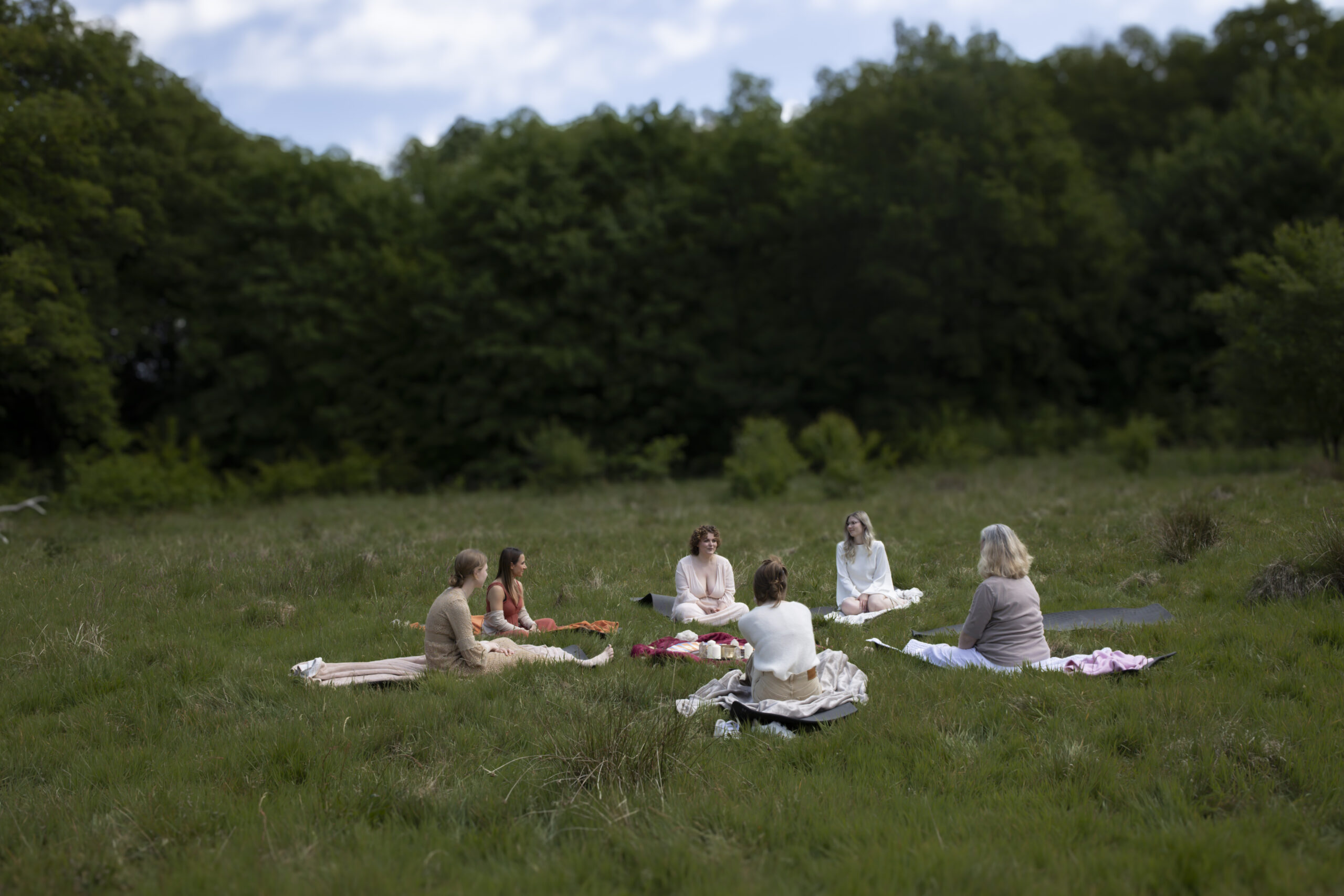 A retreat circle of women sitting together in a green meadow, photographed by Julia Bader